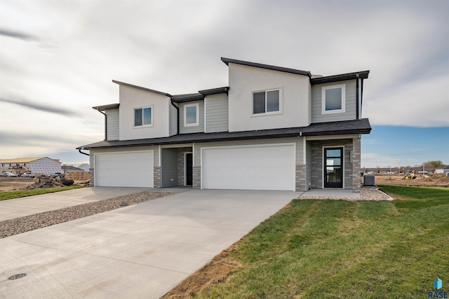 modern home with driveway, a garage, stone siding, and a front lawn