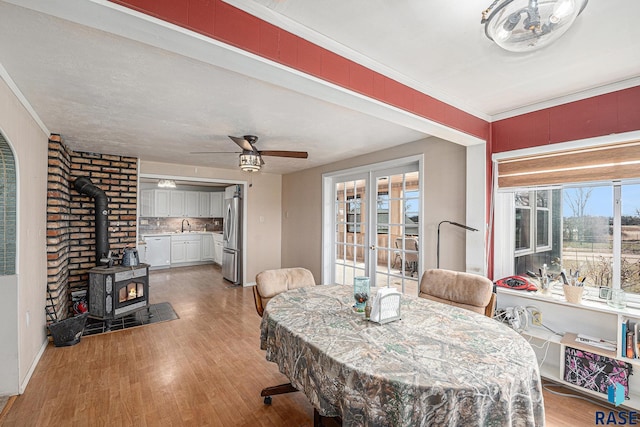 dining space featuring a wood stove, ceiling fan, crown molding, light wood finished floors, and french doors