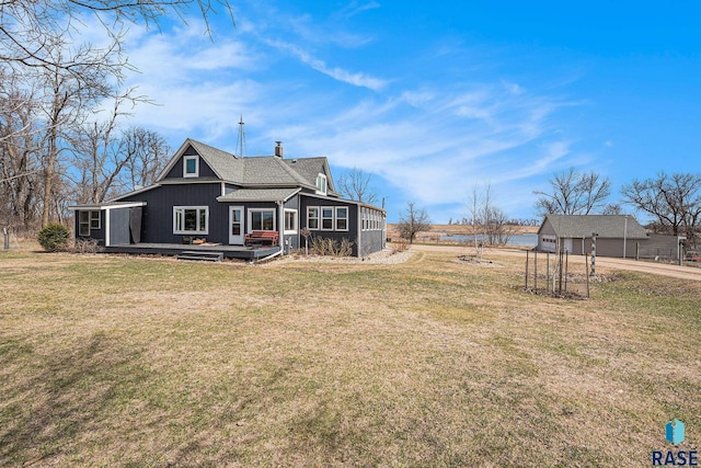 back of house featuring a chimney, a yard, a deck, a sunroom, and a shingled roof