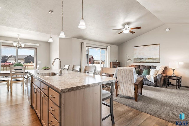 kitchen with ceiling fan, a kitchen bar, light wood-type flooring, vaulted ceiling, and a sink