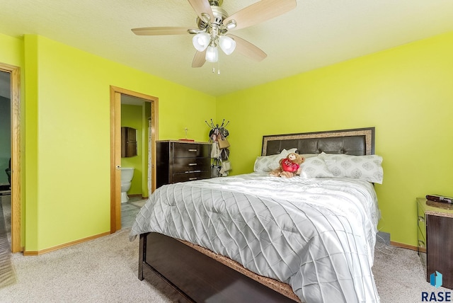 carpeted bedroom with ceiling fan, ensuite bathroom, and baseboards