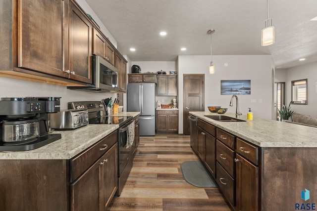 kitchen with a sink, light countertops, dark brown cabinets, wood finished floors, and stainless steel appliances