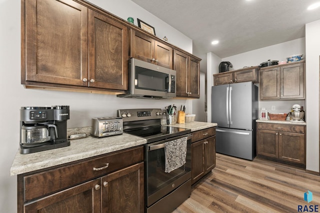 kitchen with dark brown cabinetry, recessed lighting, light countertops, light wood-style floors, and appliances with stainless steel finishes