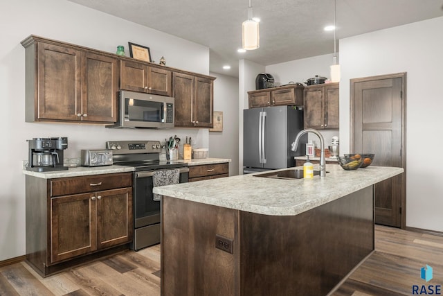 kitchen featuring appliances with stainless steel finishes, wood finished floors, light countertops, and dark brown cabinets