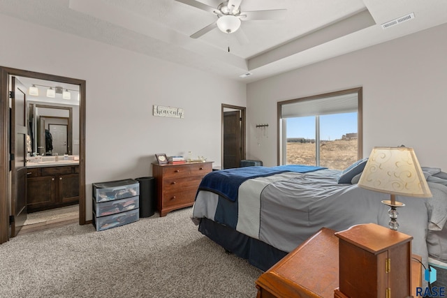 carpeted bedroom with visible vents, a raised ceiling, connected bathroom, and a ceiling fan