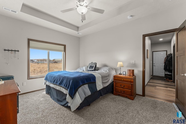 bedroom with ceiling fan, carpet, a tray ceiling, visible vents, and baseboards