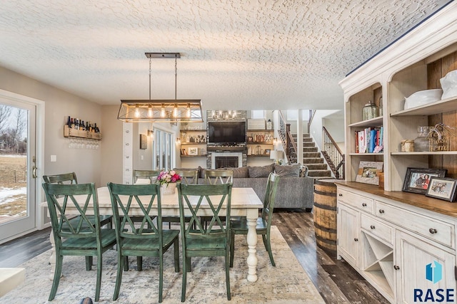 dining room with a textured ceiling, stairs, a glass covered fireplace, and dark wood finished floors