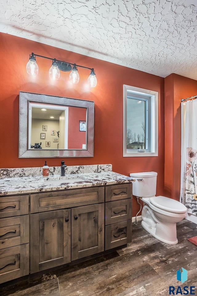 full bathroom with toilet, a textured ceiling, wood finished floors, and vanity