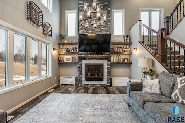 living room with a stone fireplace, an inviting chandelier, wood finished floors, and stairs