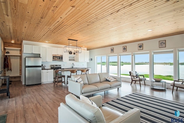 living room with a chandelier, recessed lighting, a water view, wood-type flooring, and wooden ceiling