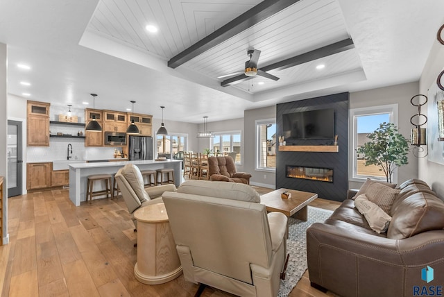 living area featuring a tray ceiling, light wood-type flooring, a healthy amount of sunlight, and a large fireplace