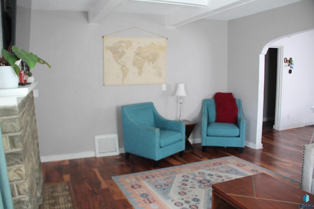 sitting room with arched walkways, wood finished floors, visible vents, and beam ceiling