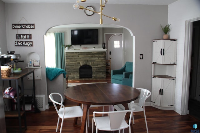 dining room with dark wood-style floors, a chandelier, arched walkways, a fireplace, and visible vents