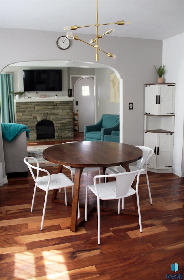 dining room featuring light wood-style flooring, a stone fireplace, arched walkways, and a notable chandelier