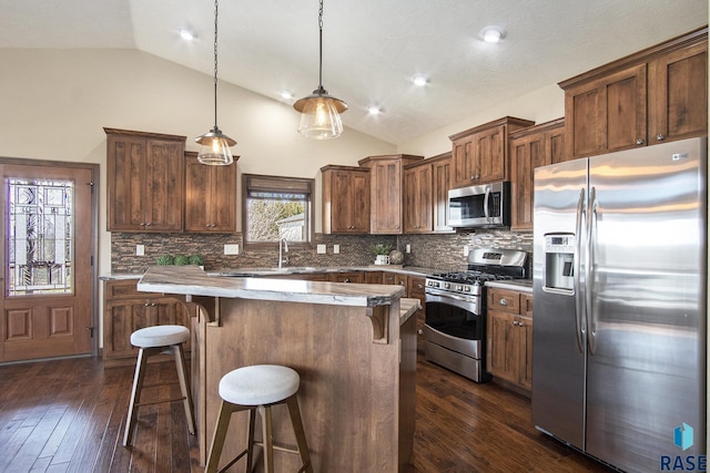 kitchen featuring dark wood-style flooring, a kitchen bar, vaulted ceiling, and appliances with stainless steel finishes