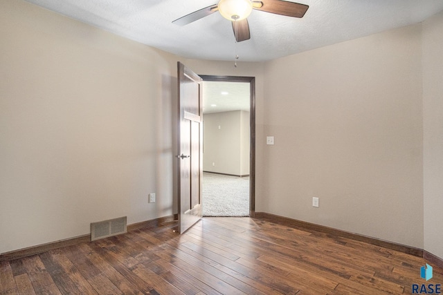 empty room with dark wood-style floors, baseboards, a ceiling fan, and visible vents