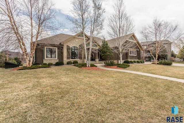 view of front of property with a front yard, roof with shingles, and stone siding