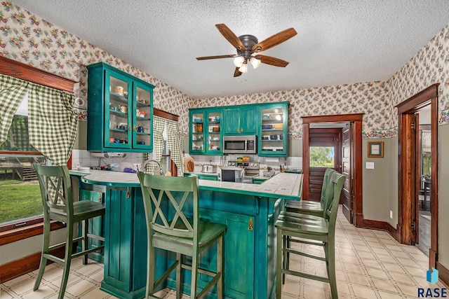 28128 462nd Ave, Davis, SD 57021 - kitchen with green cabinetry, a ceiling fan, a textured ceiling, wallpapered walls, and stainless steel appliances