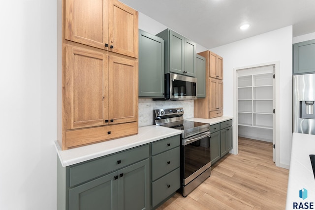 kitchen with green cabinetry, light countertops, light wood-type flooring, stainless steel appliances, and decorative backsplash