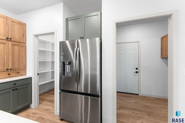 kitchen with stainless steel fridge with ice dispenser, light countertops, light wood finished floors, and baseboards