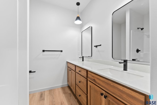 bathroom featuring baseboards, double vanity, a shower, a sink, and wood finished floors