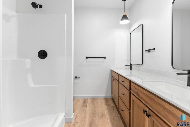 full bathroom featuring a shower stall, wood finished floors, a sink, double vanity, and baseboards