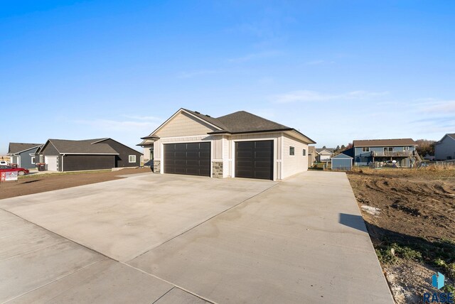view of side of property featuring an attached garage, a residential view, concrete driveway, and stone siding