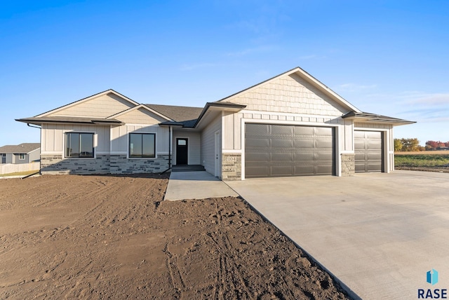 view of front of property featuring board and batten siding, stone siding, a garage, and concrete driveway