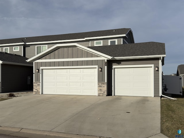 view of front of property with an attached garage, stone siding, board and batten siding, concrete driveway, and roof with shingles