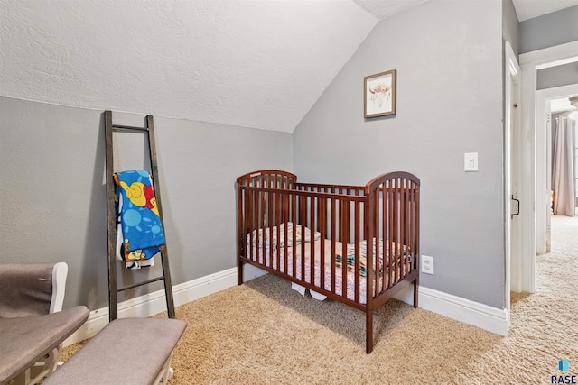 bedroom featuring a textured ceiling, a nursery area, vaulted ceiling, carpet floors, and baseboards