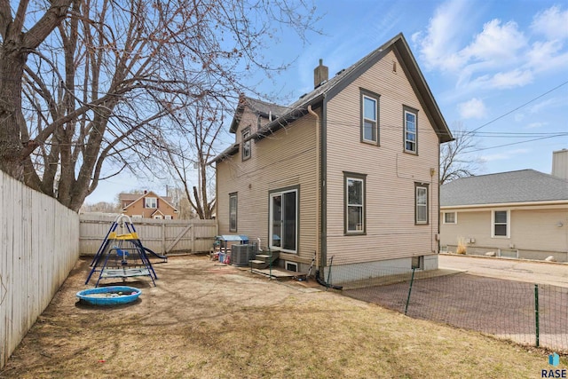 rear view of house featuring central AC unit, a playground, a fenced backyard, and a chimney
