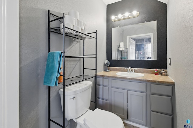 bathroom featuring toilet, a textured wall, and vanity
