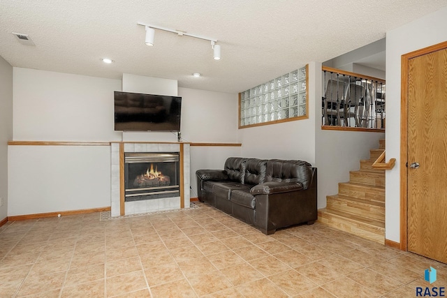 living room with track lighting, a tile fireplace, baseboards, stairway, and a textured ceiling