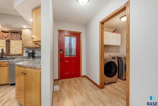 clothes washing area featuring washing machine and clothes dryer, light wood-type flooring, a textured ceiling, and baseboards