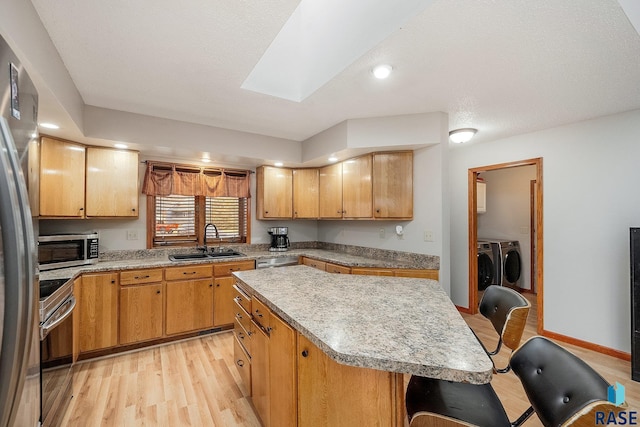 kitchen with a sink, stainless steel appliances, light wood-style floors, washing machine and clothes dryer, and light countertops