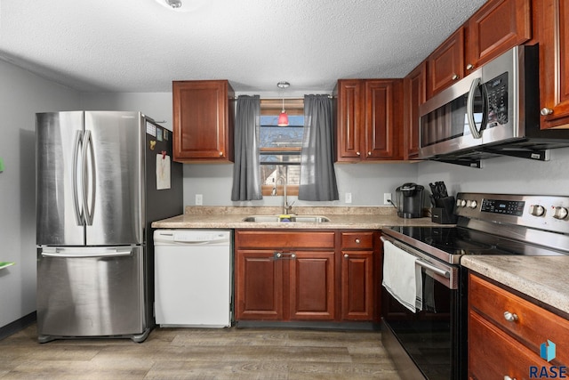 kitchen featuring stainless steel appliances, light wood finished floors, light countertops, and a sink
