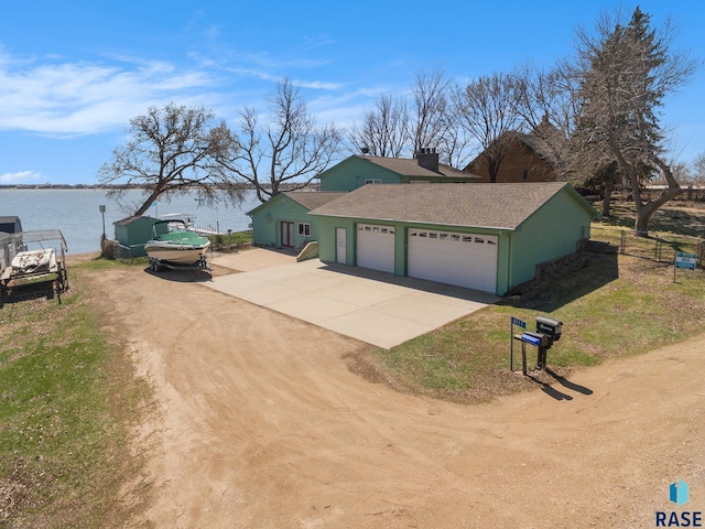 exterior space featuring a water view, an attached garage, fence, driveway, and roof with shingles