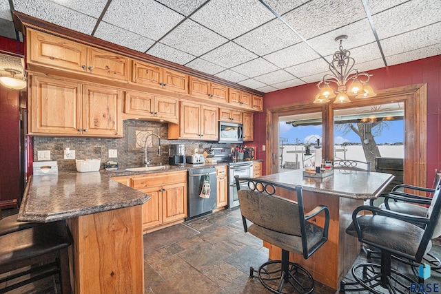 kitchen with a kitchen breakfast bar, stone tile floors, a sink, stainless steel appliances, and backsplash