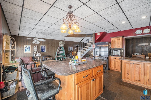 kitchen with dark stone countertops, wooden walls, a breakfast bar area, and stainless steel refrigerator with ice dispenser