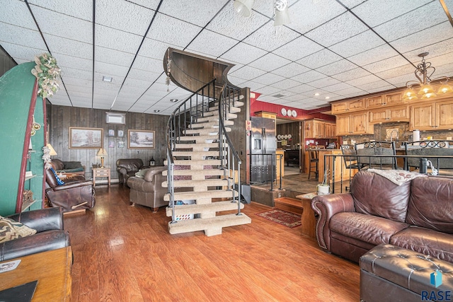 living room with stairway, light wood finished floors, a drop ceiling, and wood walls