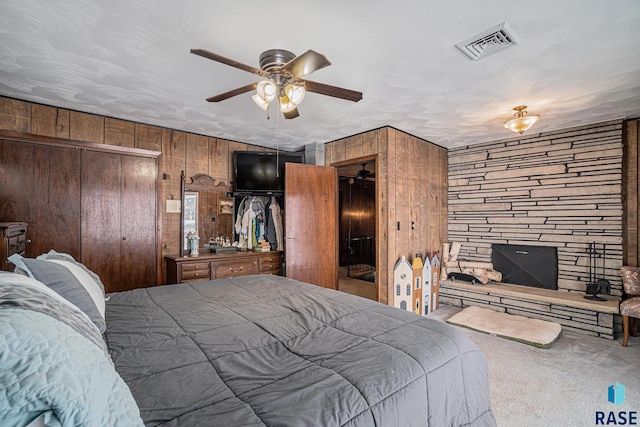 carpeted bedroom with wooden walls, visible vents, multiple closets, and ceiling fan
