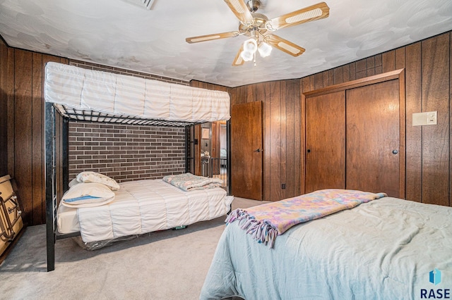 carpeted bedroom with a closet, wood walls, and ceiling fan