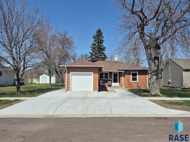 ranch-style house featuring a shingled roof, an attached garage, a chimney, a front lawn, and driveway