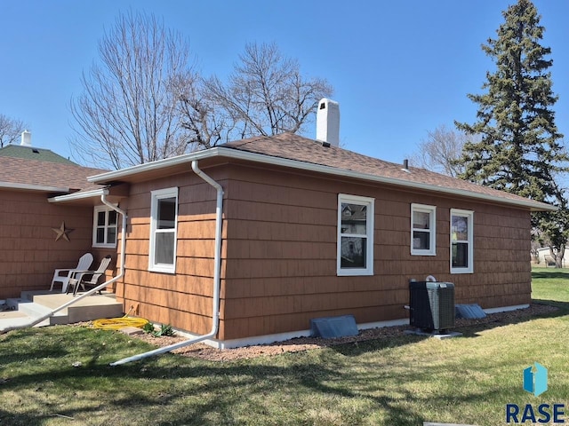 view of home's exterior featuring a shingled roof, a chimney, a lawn, and central AC