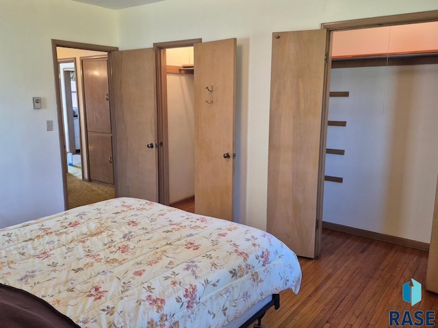 bedroom with a spacious closet, wood-type flooring, a closet, and baseboards