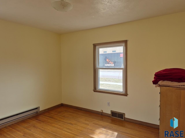 unfurnished room with baseboards, baseboard heating, light wood-type flooring, and visible vents