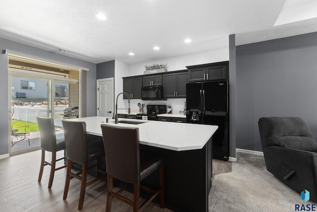 kitchen with black appliances, an island with sink, a kitchen breakfast bar, and a sink
