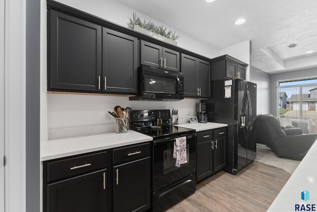 kitchen with dark cabinets, light wood finished floors, light stone counters, and black appliances