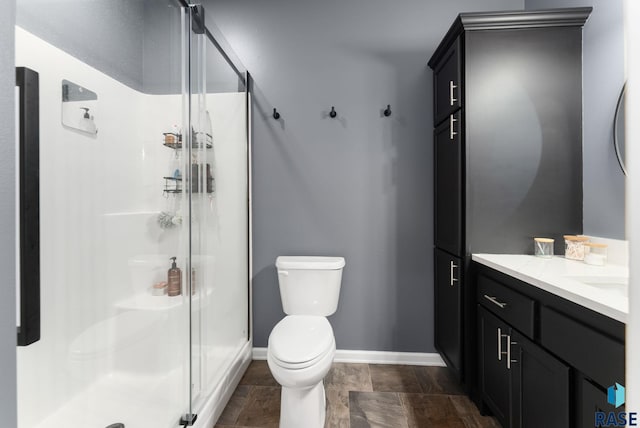 full bath featuring a shower stall, toilet, vanity, stone finish flooring, and baseboards