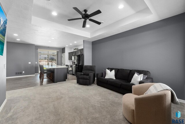 living room featuring recessed lighting, a tray ceiling, visible vents, baseboards, and carpet flooring